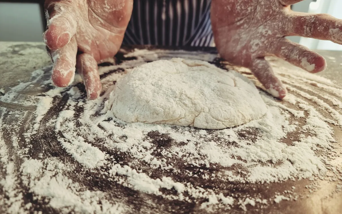 Flour-dusted hands preparing dough on a kitchen worktop.