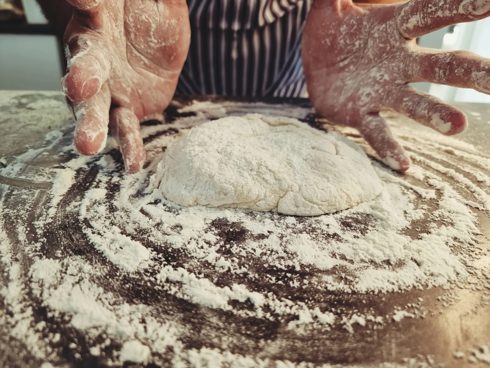 Flour-dusted hands preparing dough on a kitchen worktop.